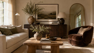 Warm organic living room with ivory linen sofa, chocolate velvet chair, oak coffee table, olive branches, and earthy neutral home decor.