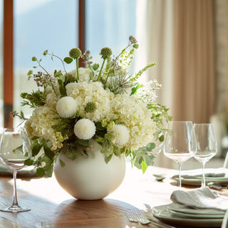 Elegant white faux floral arrangement with hydrangeas, 12" 6 Stem  mini allium, and greenery in a round ceramic vase styled on a dining table with glassware by Third & Main