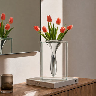13-inch clear crystal vase with sculptural polished aluminum insert styled on books atop a warm wood console with coral tulips; flowers shown are not included.