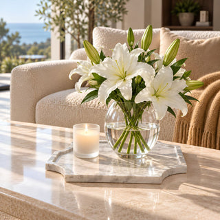 Large 14-inch natural Volakas marble tray with soft gray veining and satin finish, styled on a stone coffee table with a clear glass vase of white lilies and a candle.