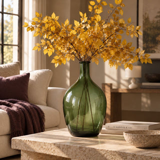 Large 19.75-inch translucent green glass bottle vase styled with tall golden fall branches on a stone coffee table in a warm neutral living room.
