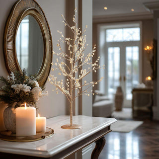 Gold glittered twig tree with pearl accents styled on marble console beside candles and mirror – elegant 24-inch tabletop holiday décor for entryway or mantel.