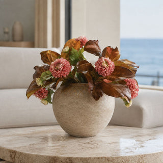 26-inch artificial bourbon magnolia leaf sprays styled with pink florals in a round stone vase on a travertine table in a light-filled living room.