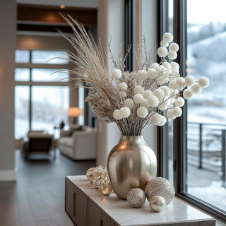 32 Inch snowy white glittered pom pom spray in a Decorative arrangement with a metallic vase and spherical ornaments on a table in a living room.