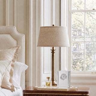 4.5-inch clear crystal table clock styled on a cream stone tray beside a brass lamp and perfume bottle on a warm wood nightstand.