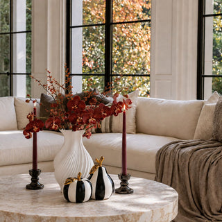 Black and white striped ceramic apple with gold leaf and stem styled on a marble coffee table with burgundy florals and candles for modern fall home decor.