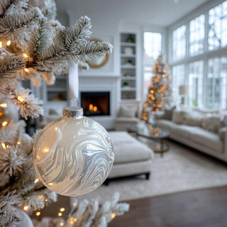 White marbled glass ornament with satin ribbon resting on snowy surface – artisan-blown 4.75-inch glass Christmas ornament for winter-white holiday styling.