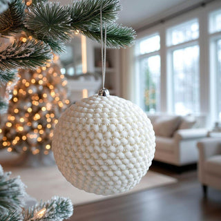 Round shaped white and gold beaded ornament on Christmas tree branch with bokeh lights in background – modern cream and gold Christmas ornament for elegant holiday styling