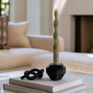 6.25-inch obsidian black glass knot sculpture styled on neutral books beside a black marble taper candle holder in a warm modern living room.