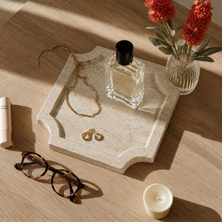 6.75 inch creamy travertine stone tray styled on a light wood surface with jewelry, perfume and a small vase for decorative catchall use.