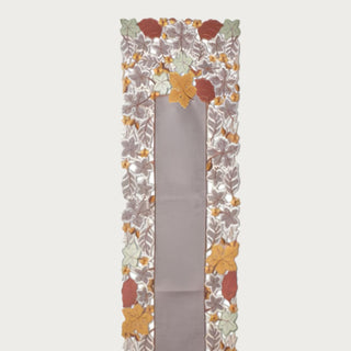 Close-up of embroidered cutout fall leaves table runner showing layered rust, ochre, sage, taupe and brown botanical detailing for Thanksgiving and autumn table styling.