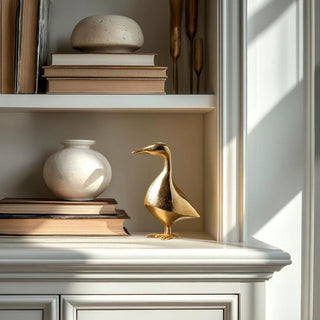 Decorative shelf with books, a white vase, and a gold duck figurine.