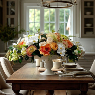 Luxurious premade faux floral arrangement with peach, apricot, and white blooms in a white pedestal vessel, styled as a statement centerpiece on a wood dining table in a quiet luxury home with natural light.