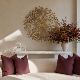 31-inch Arielle gold iron wall art styled above a marble console behind a cream sofa with merlot pillows and a fall floral arrangement.