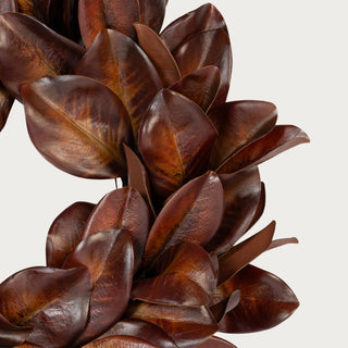 Close-up of Bourbon Brown magnolia wreath leaves showing layered cognac and mahogany tones, curved leaf shapes, and visible veining.