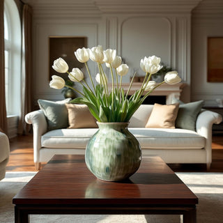 Green stoneware Brosse vase styled on a dark wood coffee table with a loose arrangement of white tulips in an upscale Southern living room with soft morning light and neutral furnishings