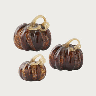 Small, medium, and large brown speckled handblown glass pumpkins shown together with amber-brown ribbed bodies and champagne-gold looping stems.