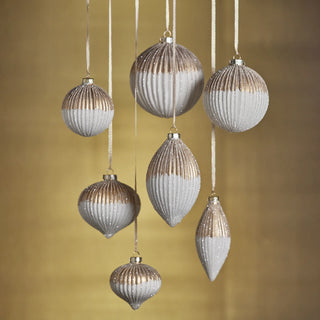 Collection of matte cream and gold ribbed glass ornaments in assorted shapes hanging against gold backdrop – timeless modern holiday ornaments for luxury holiday decorating.