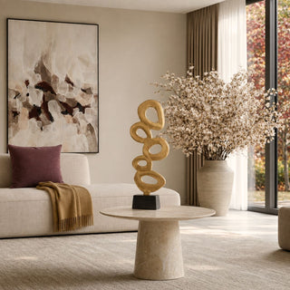 23 Inch Contour Gold Sculpture styled on a round stone coffee table in a warm contemporary living room with neutral upholstery, abstract art, and a large floral arrangement.