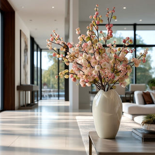 Styled floral arrangement featuring faux crabapple stems with blush berry clusters in a sculptural ceramic vase, placed on a console table in a light-filled modern living space.