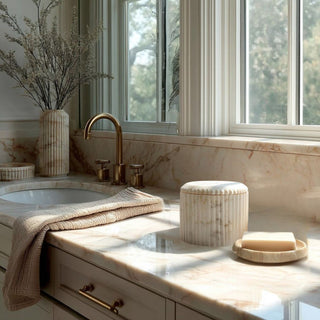 cream marble bathroom accessories set with ribbed canister soap dispenser and dish styled on marble countertop with brass faucet and neutral decor in natural light