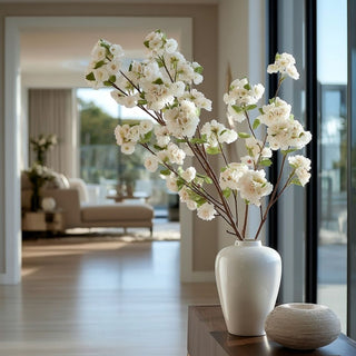23.5-inch True Bloom creamy white real touch blossom stems arranged in a tall ivory vase in a bright modern contemporary living room with floor-to-ceiling windows and natural light.