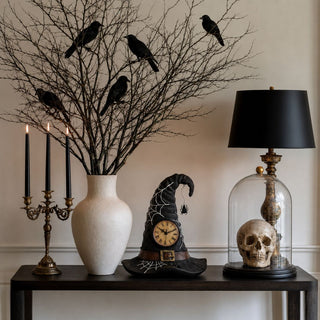 11.5 Inch Decorative Resin Witch Hat styled on a Halloween console with bare branches, black birds, black taper candles, skull decor, and moody seasonal accents.