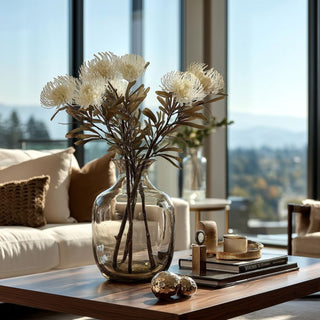 Glass vase with faux white spike cactus dahlia stems styled on modern coffee table in sunlit living room.