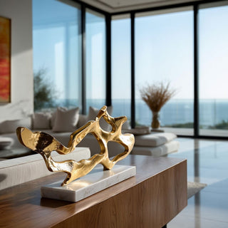 Gold abstract Cohen sculpture with textured finish resting on white marble base styled on walnut console table in luxury modern contemporary coastal home with floor-to-ceiling windows and ocean view, refined sculptural decor by Third & Main