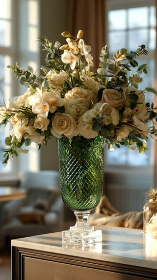 Decorative floral arrangements True Bloom Real Touch Florals  in a green glass vase on a table with a blurred indoor background