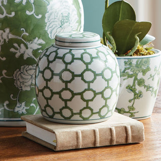 Green and ivory ceramic ginger jar with woven trellis pattern and classic rounded lidded resting atop a neutral color book and complimentary green and white vessels behind