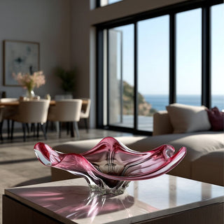 22-inch handblown rose and clear art glass bowl styled on a marble coffee table in a modern coastal luxury living room with floor-to-ceiling windows and ocean views.