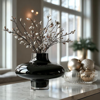 Handmade onyx black glass vase with sculptural round silhouette styled on marble countertop holding frosted winter branches, surrounded by gold and silver ornaments in a bright modern living room – elegant holiday home décor inspiration with modern glass accents.