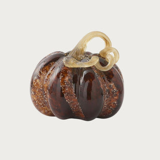 Large brown speckled handblown glass pumpkin measuring 8 inches high by 9 inches wide with amber tones and a looping champagne-gold glass stem.