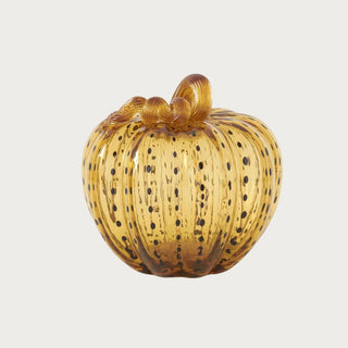 Large handblown golden amber glass pumpkin measuring 7.5 inches high and 7.75 inches wide with dark speckling and a looping glass stem.