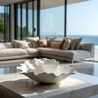 Modern white ceramic statement bowl with organic flowing silhouette displayed on a travertine coffee table in a luxury Malibu California contemporary home with coastal ocean backdrop.