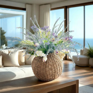 Lavender Meadow Tulip Arrangement Bundle featuring white and lavender real-touch mini tulips, white lily of the valley, and Dusty Sage and Lavender Meadow Sprays styled in a round woven seagrass vase on a wood coffee table in a modern transitional living room with warm natural light.