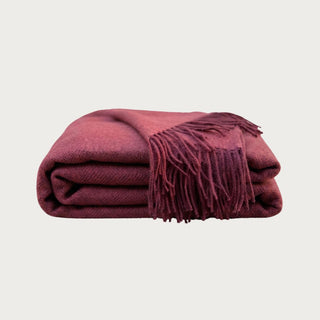 Close-up of the Malbec 100% baby alpaca throw showing its soft woven texture, rich wine-red color and coordinating fringed edge.