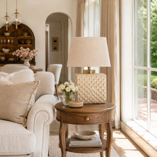 cream woven porcelain table lamp with linen shade styled on wood side table in bright neutral living room with warm natural light