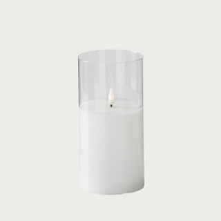 Medium white LED flickering flameless candle in clear glass cylinder on neutral background, 7 inches high by 3 inches wide, battery-operated with 5-hour timer — modern ambient lighting for shelves, side tables, and dining settings.