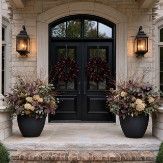 Two merlot magnolia leaf wreaths styled on black double front doors with large planters of cream, eucalyptus, and burgundy fall foliage.