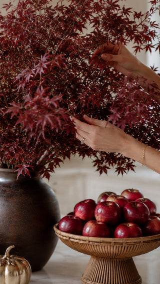 Woman's hands re-arranging a large bouquet of red maple leaf faux stems in a modern but traditional high end kitchen