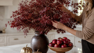 Woman's hands re-arranging a large bouquet of red maple leaf faux stems in a modern but traditional high end kitchen