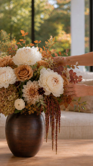 Woman re-arranging a lush luxe floral arrangement from True Bloom Floral which is sitting in the dark wood medium sized vase in a sunny california home