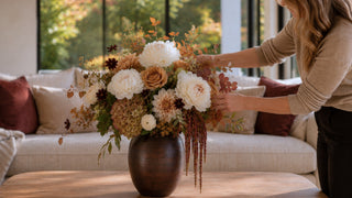 Woman re-arranging a lush luxe floral arrangement from True Bloom Floral which is sitting in the dark wood medium sized vase in a sunny california home