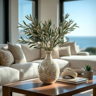 Decorative vase with olive stem greenery on a coffee table in a living room with a view of the ocean.
