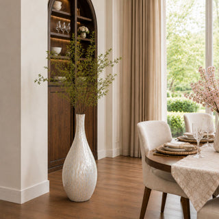 A softly layered luxury dining space featuring a luminous mother of pearl floor vase, warm wood finishes, and abundant natural light designed to feel elevated yet effortlessly livable.
