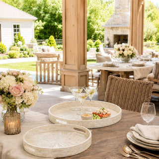 round mother of pearl serving trays styled with cocktails and appetizers on outdoor dining table in luxury covered patio setting