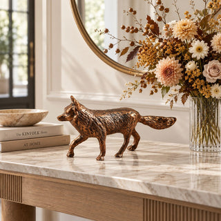 Mr Fox 10-inch cast aluminum fox sculpture with an antique gold-bronze finish and detailed walking silhouette, styled on a stone-top wood console beside neutral books and a floral arrangement.