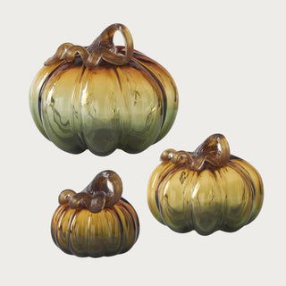 Small, medium, and large ombre glass pumpkins showing transparent amber-to-olive green color, ribbed sides, and curled brown glass stems.